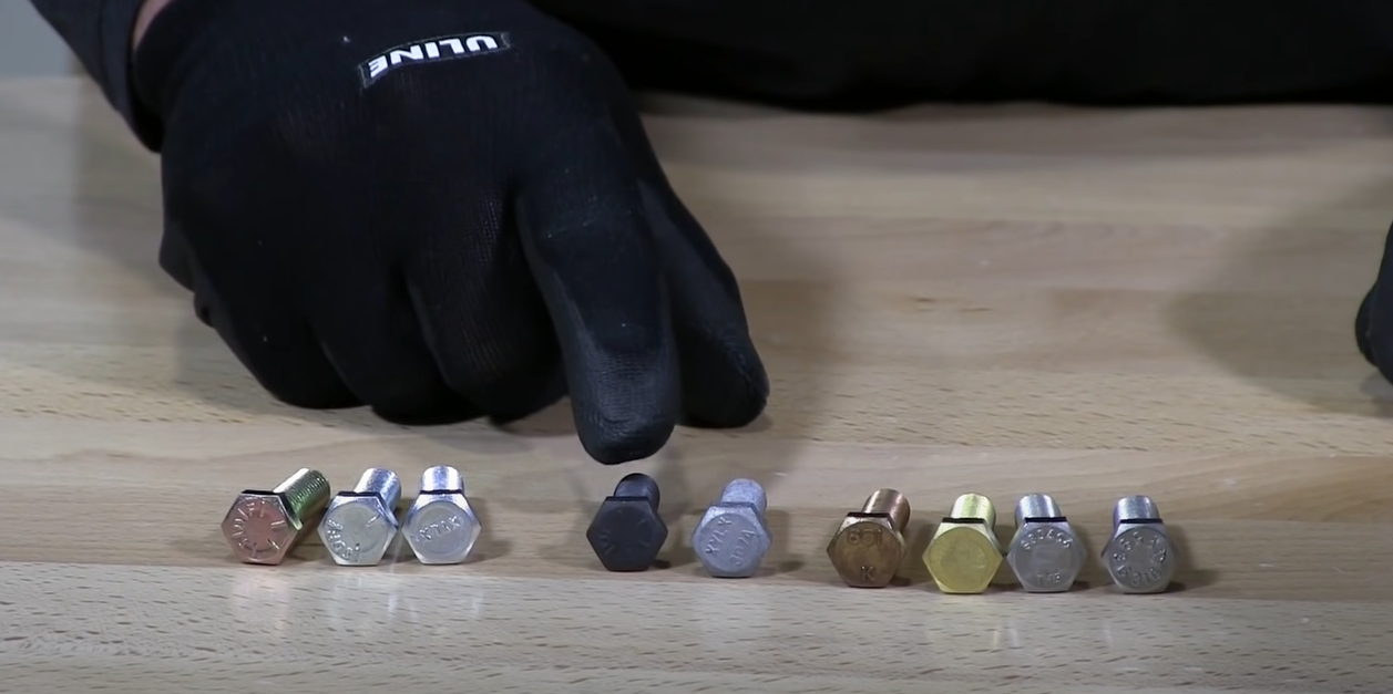 Various bolts on a table with a gloved hand pointing at one bolt