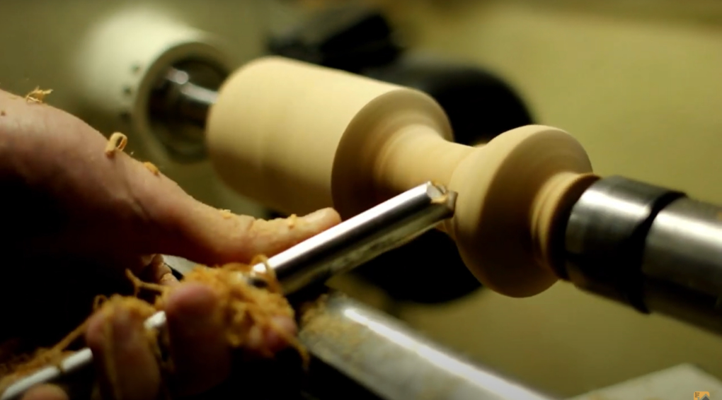 A man carves a figure out of wood on a lathe