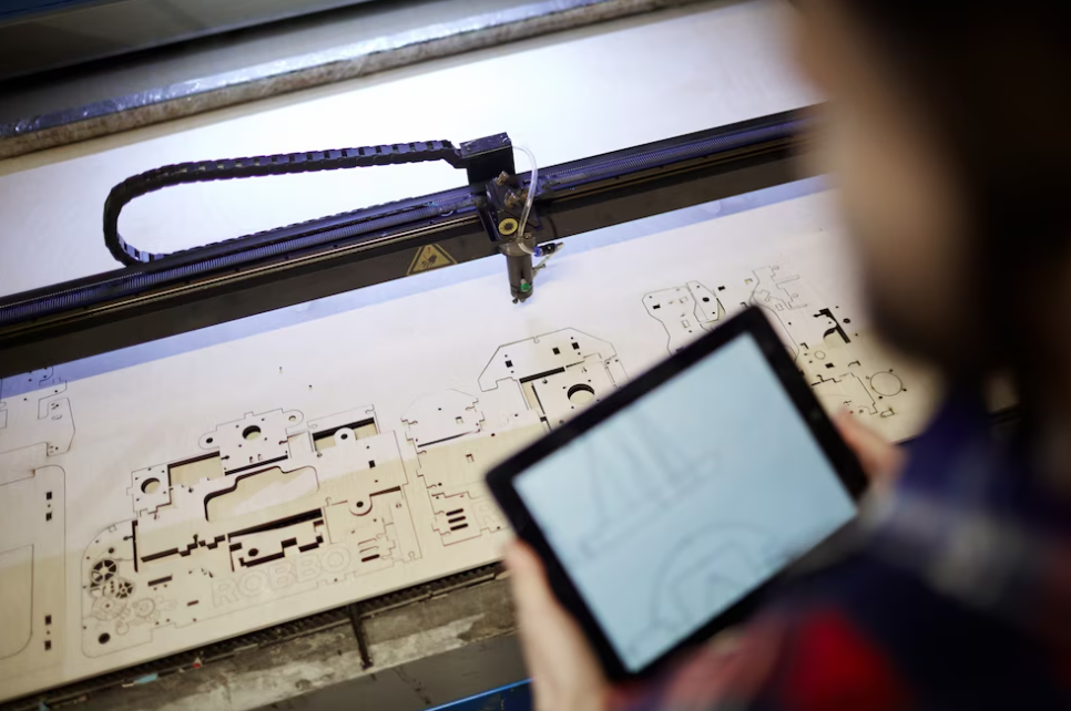 man holds a tablet and looks at the CNC machine drawing