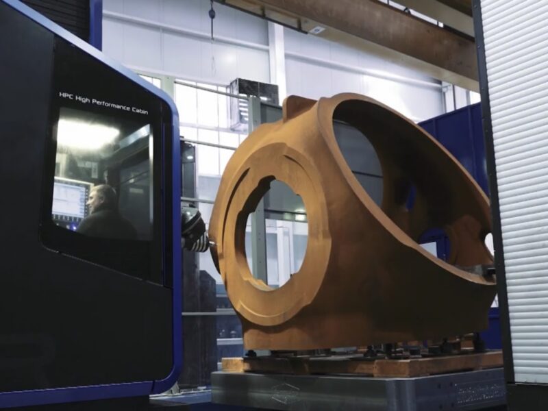 A precision engineering machine with a large brown metallic part secured on the table, within an enclosed blue cabin