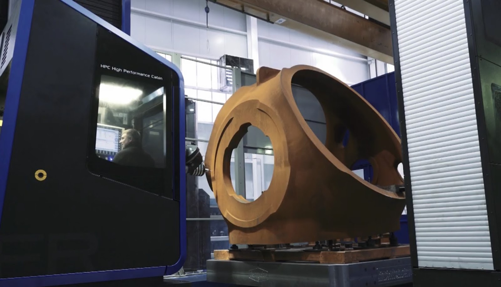 A precision engineering machine with a large brown metallic part secured on the table, within an enclosed blue cabin